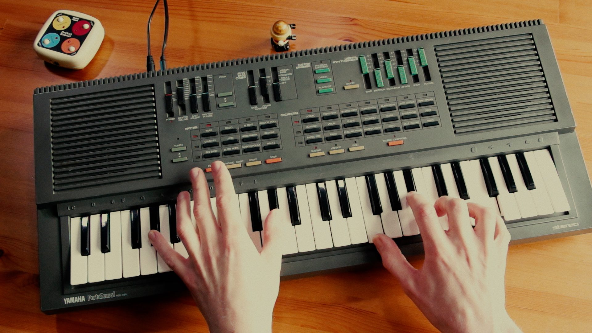 A small robot walking past a Yamaha PSS-460 with an 80s memory game in the background