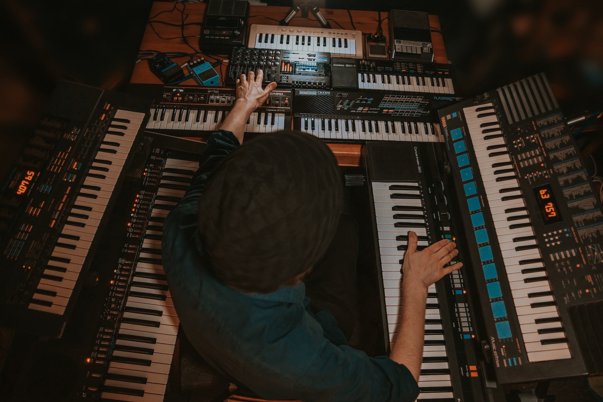 Alfonse surrounded by vintage keyboards, pushing buttons and moving the fader on a 4-track tape recorder